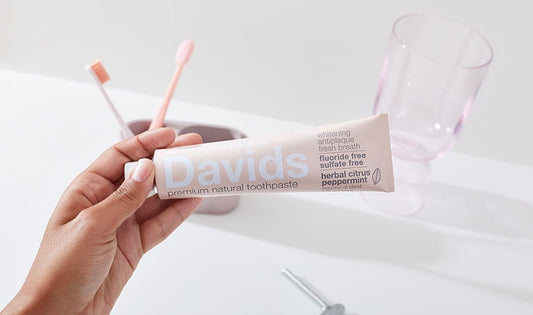 Davidsのピンク色の歯みがき粉のチューブを持つ手と、コップに立てた歯ブラシ