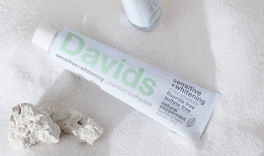 白いタオルの上に置かれたDavids Hydroxi™ ホワイトニングトゥースペースト（センシティブ）と白い石
