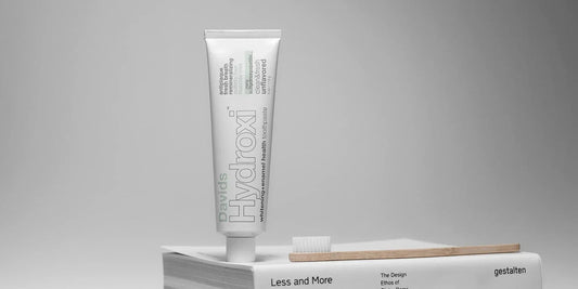 本の上に置いたDavids Hydroxi™ の歯みがき粉のチューブとバンブー歯ブラシ